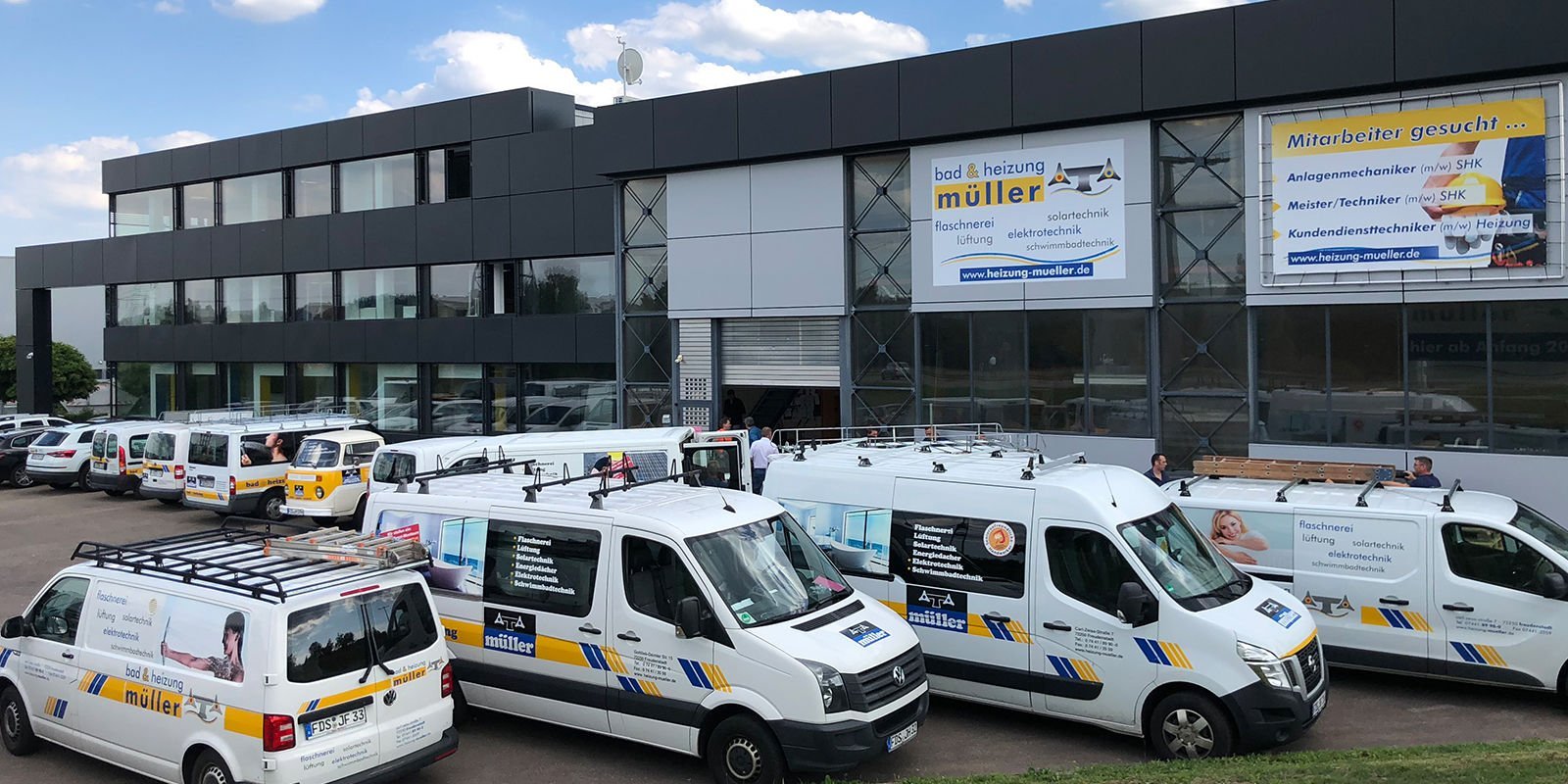 Eine moderne Firmengebäude mit großen Fenstern, umgeben von mehreren Lieferwagen, die für Sanitär- und Heizungsdienste genutzt werden.