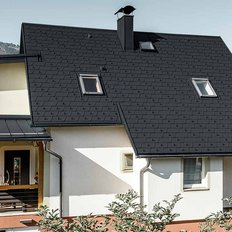 Ein modernes Haus mit einem schwarzen Dach, umgeben von sanften Hügeln und Bäumen, strahlt Ruhe und Eleganz aus.